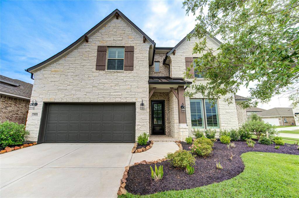 Charming stone facade with a welcoming front porch, complemented by lush landscaping and a spacious driveway.