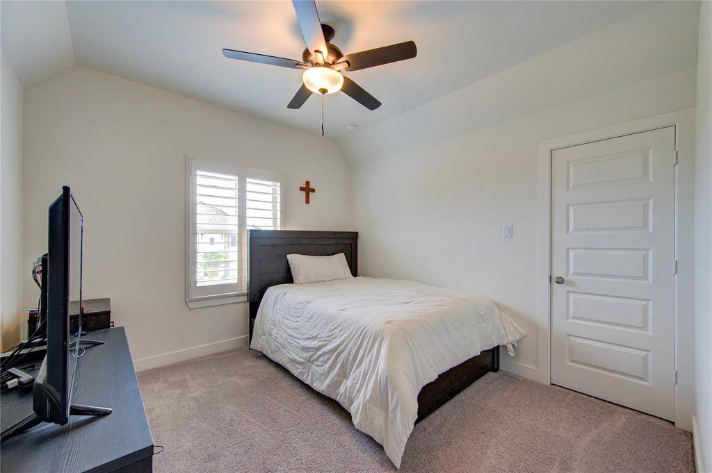 Cozy bedroom featuring plush carpet, modern ceiling fan, and  natural light through elegant shutters. Perfect for relaxation.