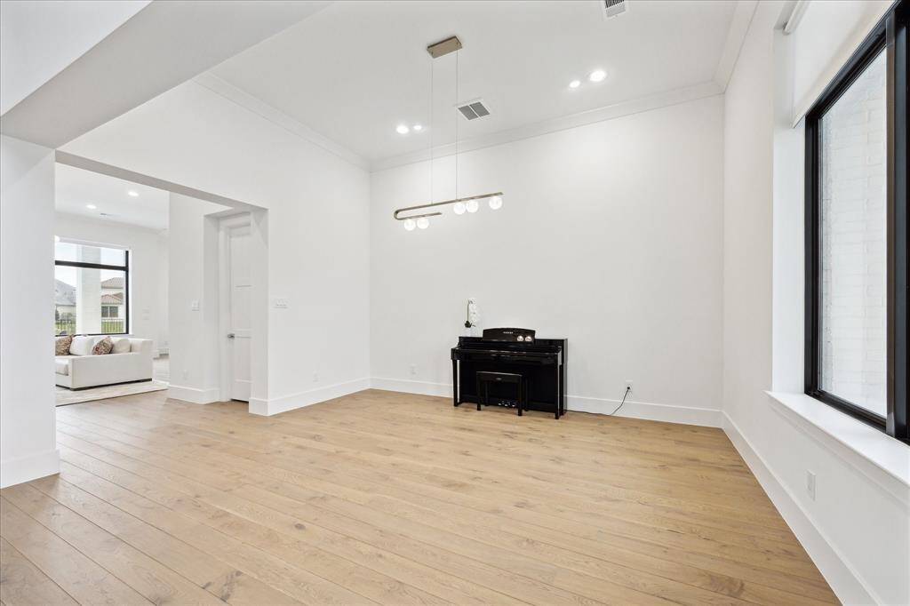 The formal dining room, currently serving as a piano room, is enhanced by exquisite designer lighting. It offers ample space for hosting a formal gathering, whether for a special occasion or holiday celebration.