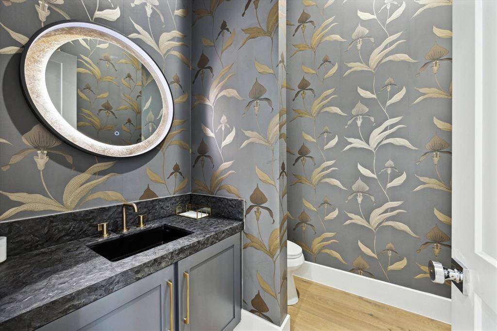 The first-floor powder bath is elegantly designed with custom wallpaper and a sleek light-up mirror.