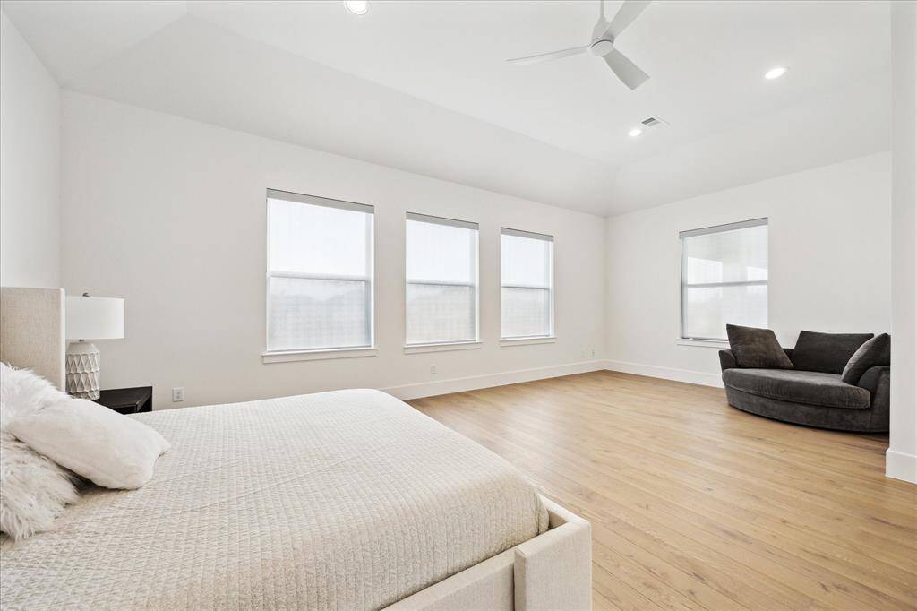 The primary bedroom features a cozy seating area, soaring high ceilings, and an abundance of windows, creating a light-filled, bright, and inviting retreat.