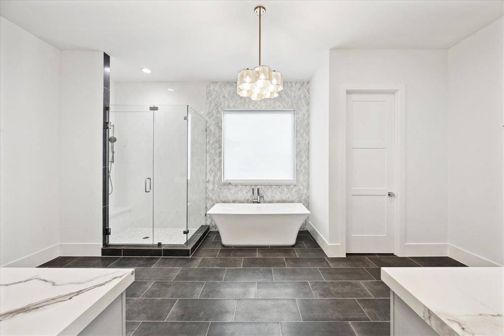 The primary bath is designed with a freestanding tub and a frameless glass shower featuring a handheld showerhead, offering a spa-like experience.