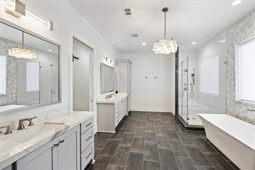 The primary bath boasts dual vanities with sleek quartz countertops, linen cabinets, designer lighting, and beautiful tile floors, offering a touch of luxury, along with a Toto soft-close bidet seat for added comfort.