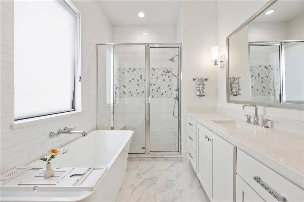 The secondary en suite bathroom features a standalone tub and separate shower adorned with decorative tile, a quartz-topped vanity, and a convenient linen closet for added storage.