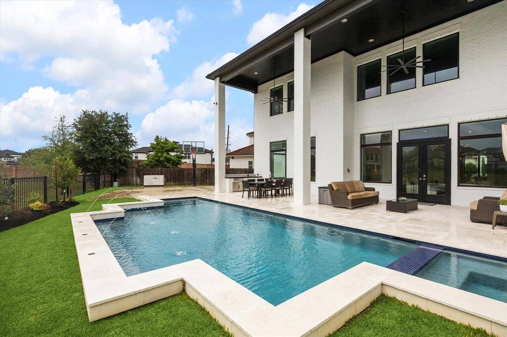 The pool features soothing laminar water jets, a saltwater system, PebbleTec finish, built-in benches, and a relaxing spa, all set against elegant travertine decking, creating a truly luxurious outdoor oasis.