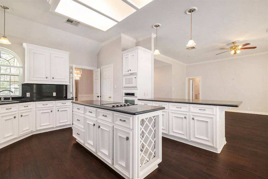 The beautifully designed kitchen features sleek white cabinets, a built-in wine rack, a big center island with a cooktop, breakfast bar seating, and a breakfast nook.