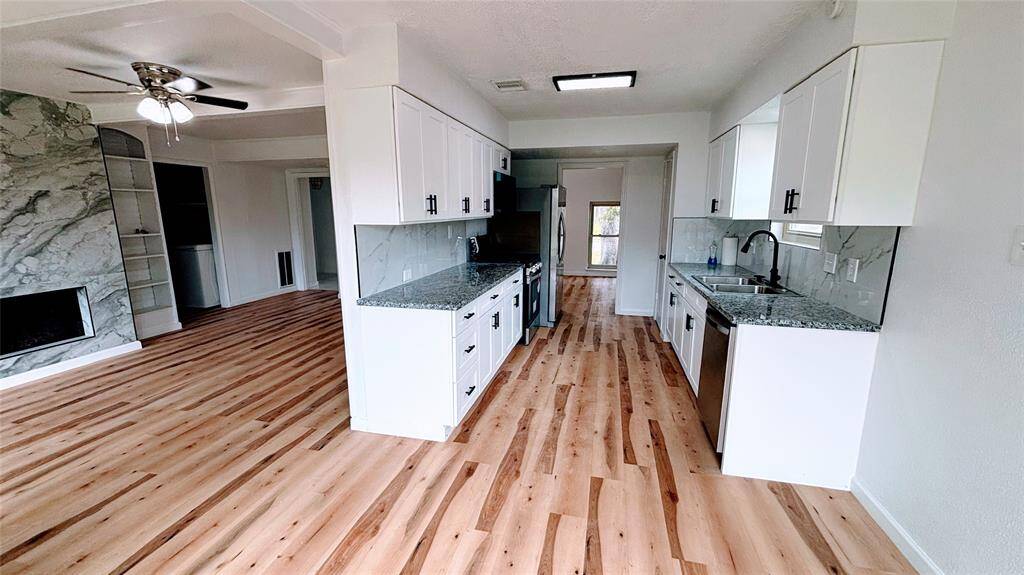 The bright, open-concept kitchen and living area. The kitchen features modern white cabinets, granite countertops, and stainless steel appliances.