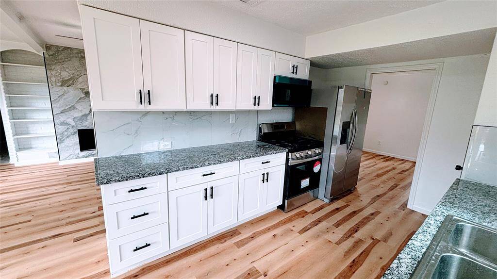 The bright, open-concept kitchen and living area. The kitchen features modern white cabinets, granite countertops, and stainless steel appliances.