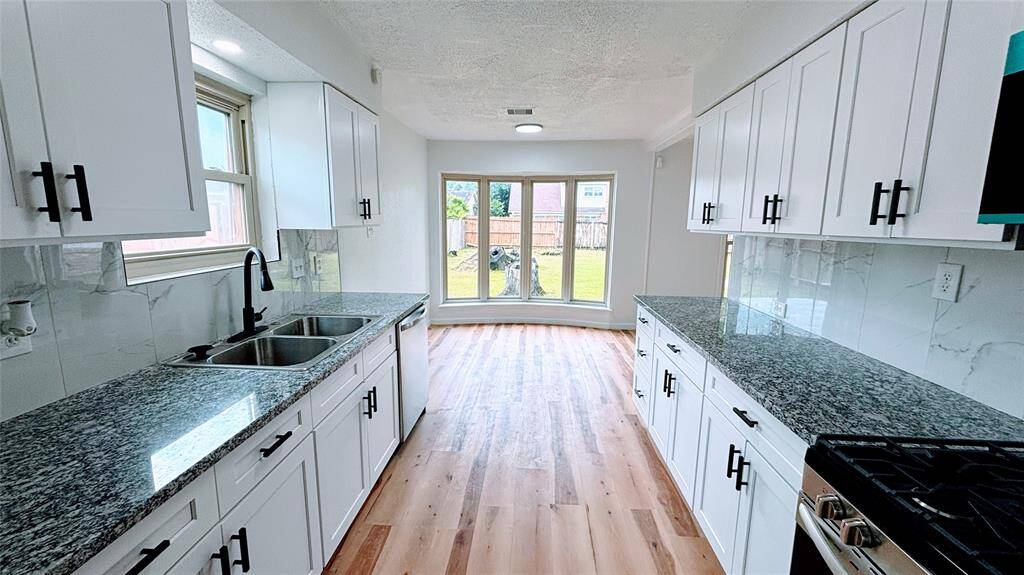 Bright kitchen with modern white cabinets, granite countertops, and stainless steel appliances. The space features large windows overlooking the backyard.