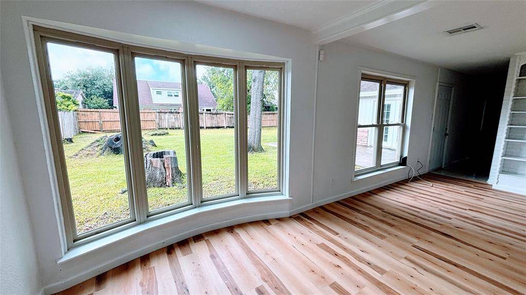 Bright room with expansive windows offering a view of a fenced backyard with mature trees.