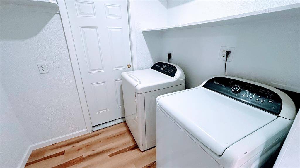 Bright and functional laundry room with hardwood flooring. It features a washer and dryer set, ample countertop space, and a utility door for easy access.