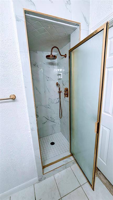 Modern  shower with a frosted glass door, marble-style tile, and bronze fixtures.