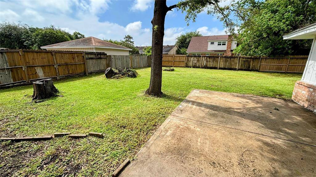 Spacious backyard featuring a grassy lawn, a large tree, and a concrete patio area.