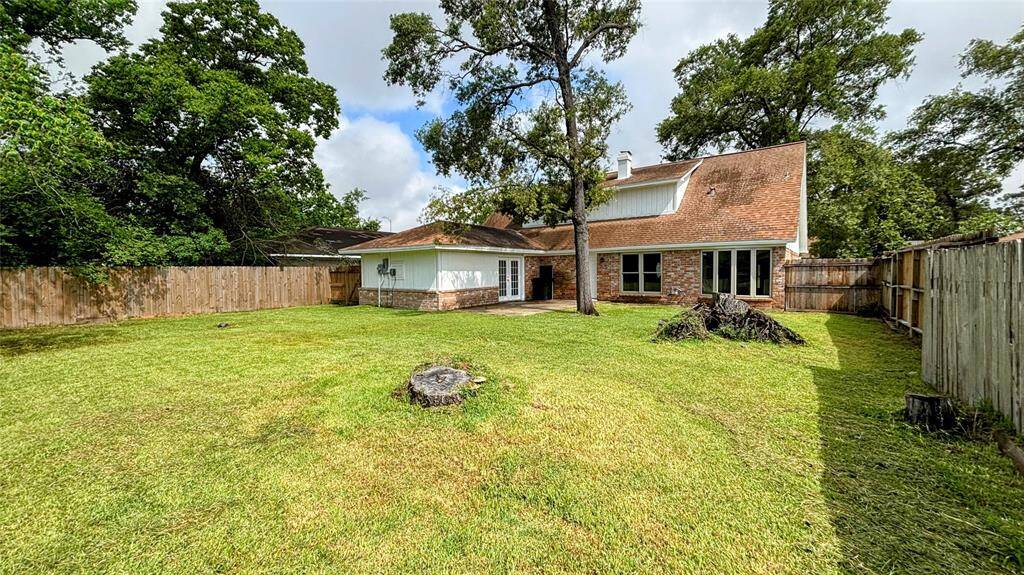 Spacious backyard featuring a grassy lawn, a large tree, and a concrete patio area.