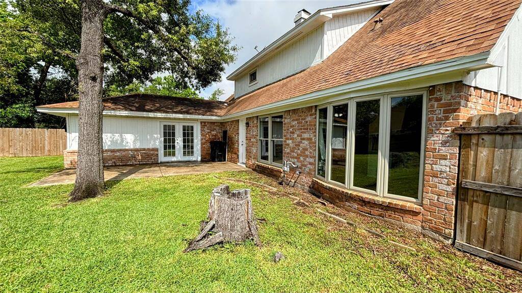 Spacious backyard featuring a grassy lawn, a large tree, and a concrete patio area.