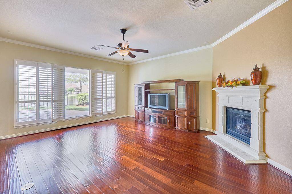 Living room features hand scraped, cherry wood floors, cast stone fireplace, and Plantation shutters on the window. High ceiling and wall of windows draw in lots of natural light.