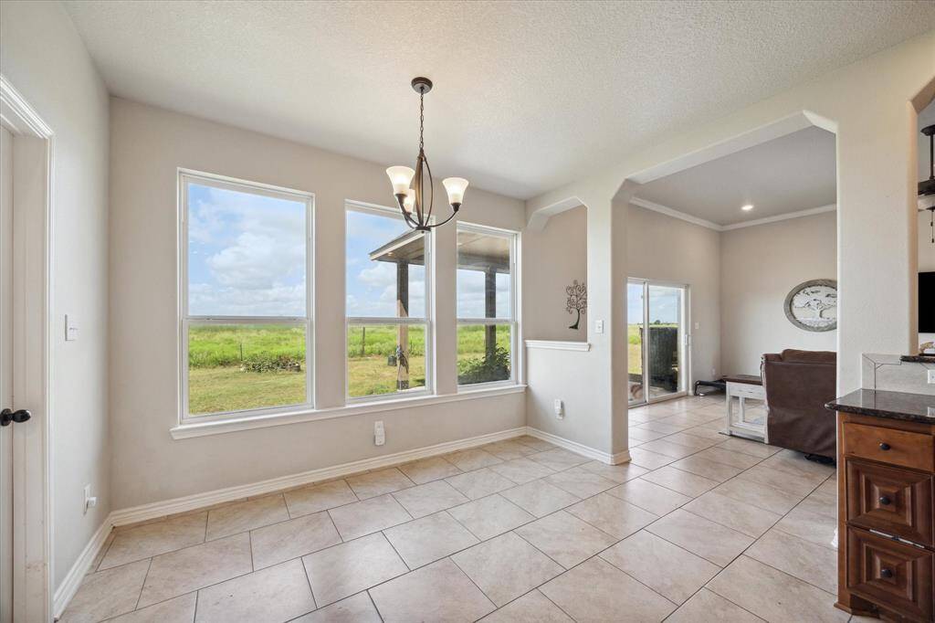 This is a bright, spacious breakfast room featuring tiled flooring, large windows with a pastoral view, and an elegant chandelier.