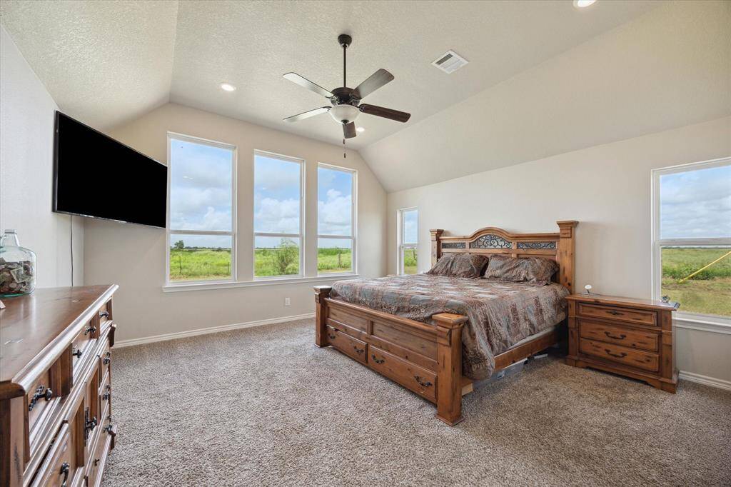 This is a spacious Primary Suite with carpeted flooring, and large windows offering a view of the open landscape. The room also features a ceiling fan and recessed lighting.