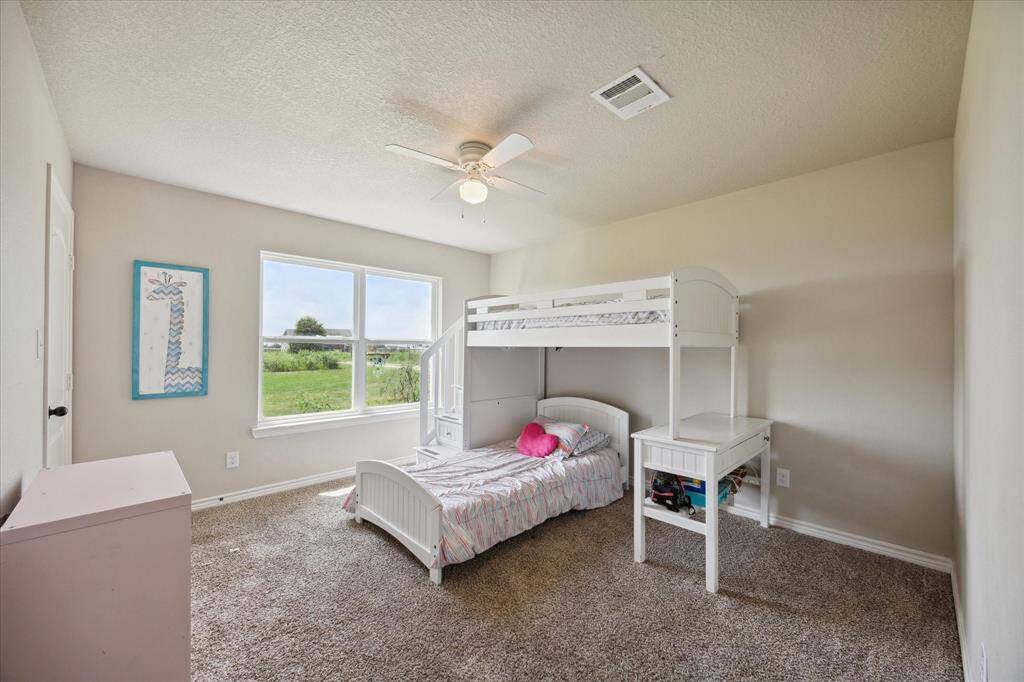 Bedroom features neutral walls and carpet, with ample natural light from a large window offering a pleasant view.