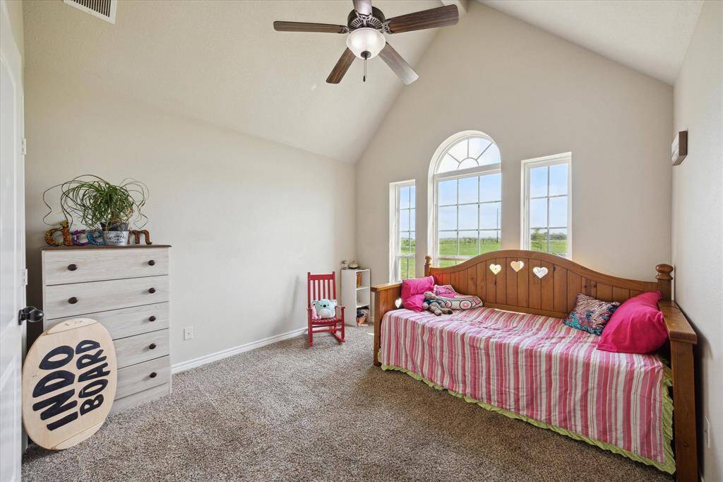 This is a bright, spacious bedroom featuring large arched windows, high ceilings with a fan, and cozy carpeting.