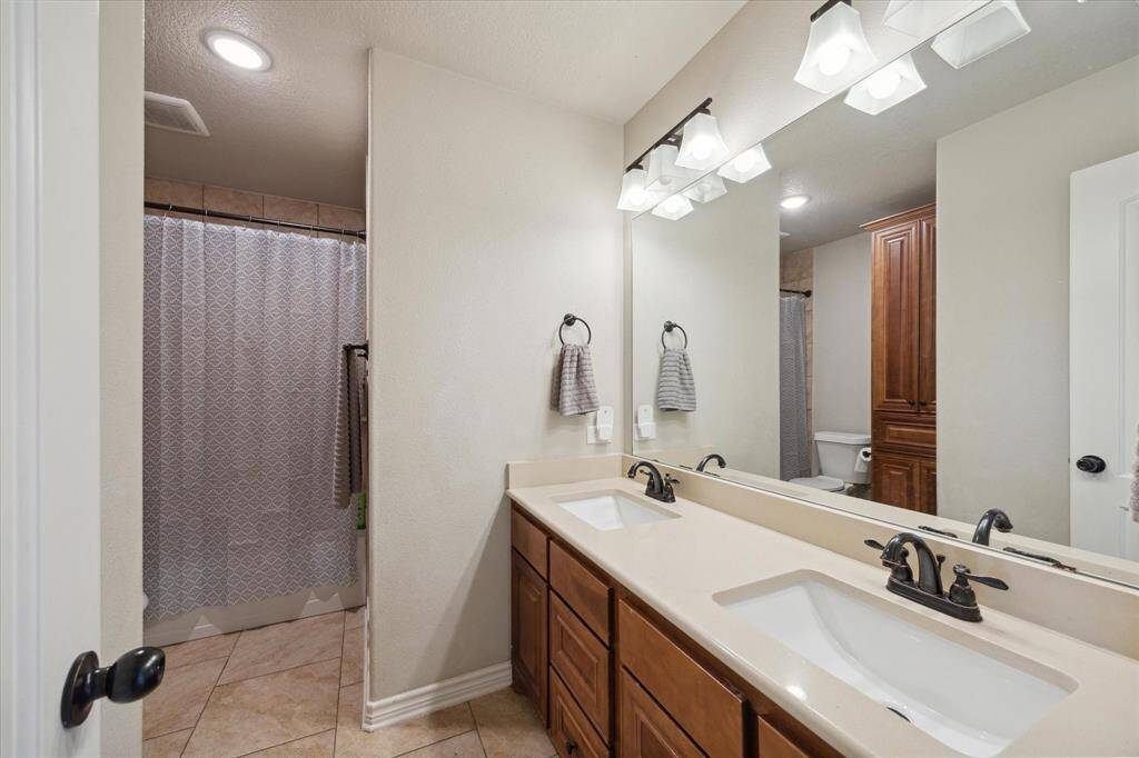 Bathroom featuring a dual-sink vanity with ample storage, a large mirror with modern lighting above, and a full bathtub/shower combo. The space is finished with tile flooring.