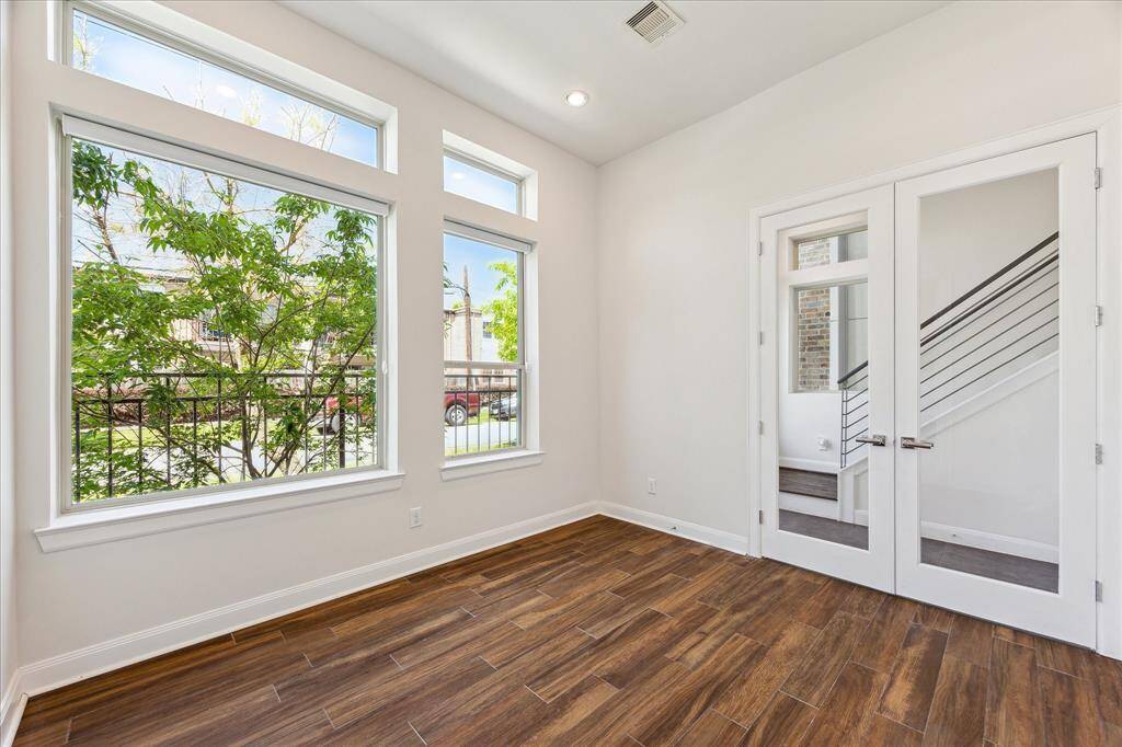 First-floor bedroom features neutral-toned French doors, offering flexibility as a private office or cozy guest suite.