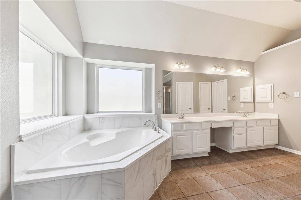 SPACIOUS PRIMARY BATHROOM FEATURING A LUXURIOUS JETTED TUB WITH LARGE WINDOWS THAT ALLOW NATURAL LIGHT.