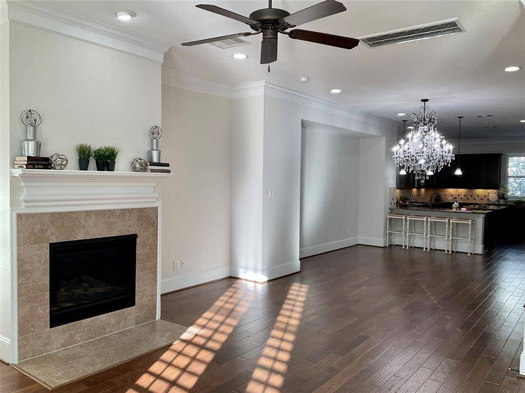 A lovely open living space with hardwood floors, a cozy fireplace, and a ceiling fan. The adjacent kitchen features a modern chandelier, a bar with seating, and ample natural light. Perfect for comfortable living and entertaining.