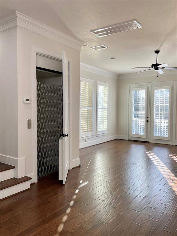 Bright and inviting 2nd floor living space with hardwood floors, abundant natural light through large windows and glass doors, a ceiling fan, crown molding, and an accessible elevator.