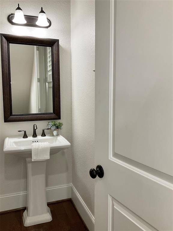 Your guest bath on the 2nd floor is a compact, stylish half-bathroom with a pedestal sink, a dark-framed mirror, and modern light fixtures. The neutral color palette and wood flooring create a clean, inviting space.