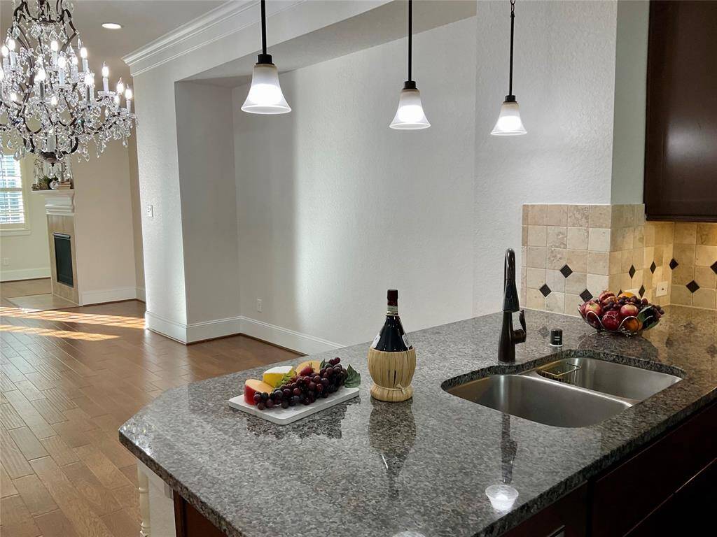 A modern kitchen with granite countertops, a double sink, and stylish pendant lighting. Adjacent is a dining area featuring a grand chandelier and hardwood floors, leading to a cozy fireplace. Ideal for entertaining and family gatherings.