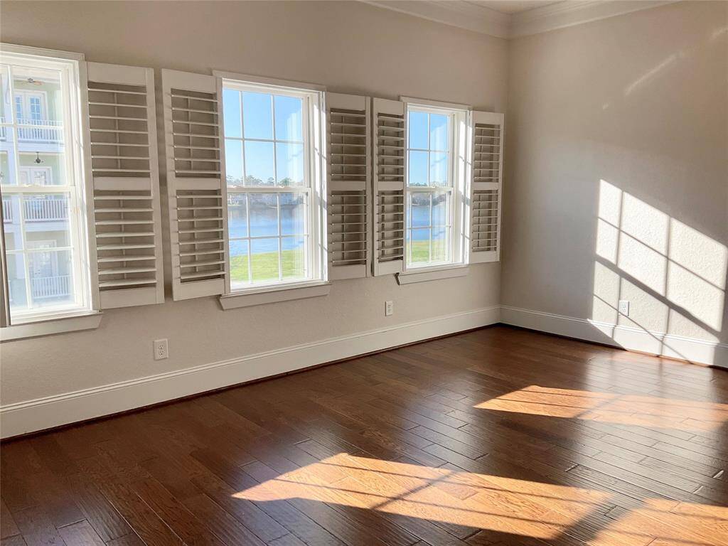 Bright, primary bedroom with large windows featuring plantation shutters, offering a beautiful lakeside view. Hardwood floors enhance the warm, inviting atmosphere.