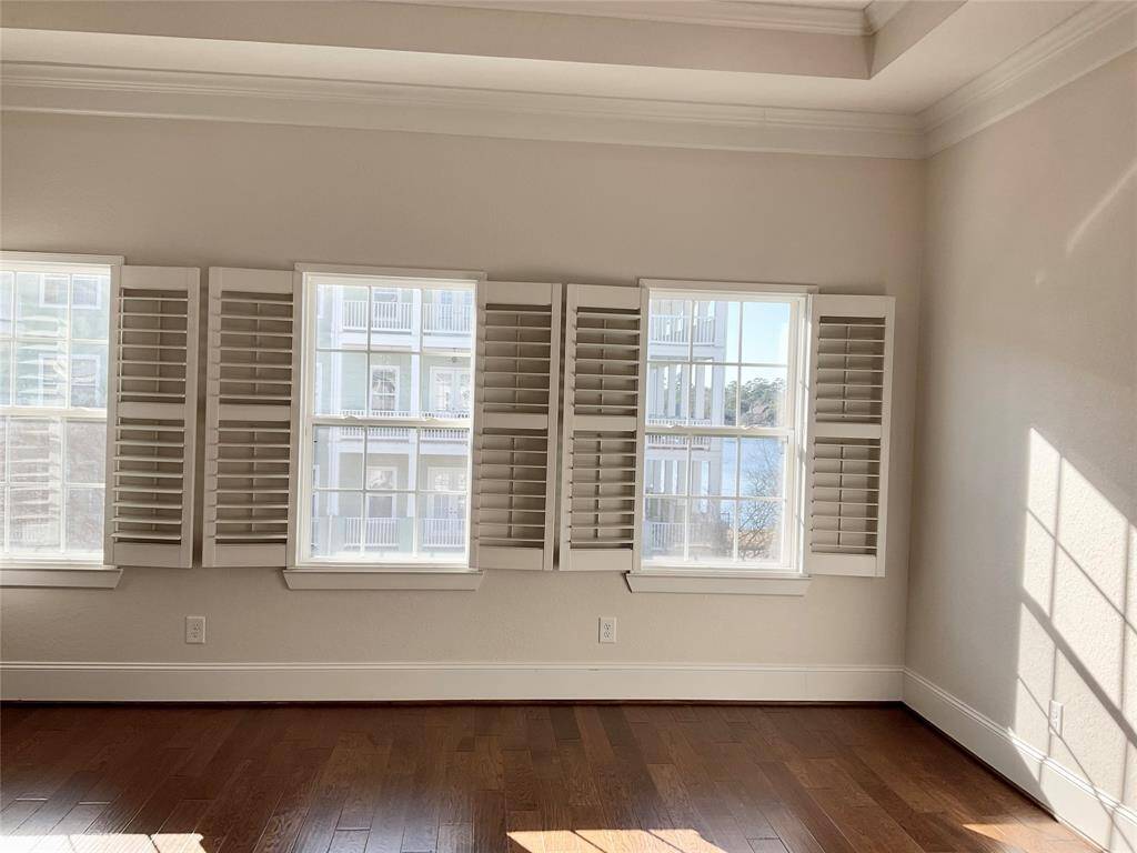 Bright, primary bedroom with large windows featuring plantation shutters, offering a beautiful lakeside view. Hardwood floors enhance the warm, inviting atmosphere.