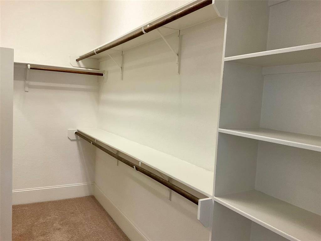 This photo shows a spacious walk-in closet featuring multiple shelves and hanging rods, ideal for organized storage. The neutral colors and ample space provide a versatile and functional area for clothing and accessories.