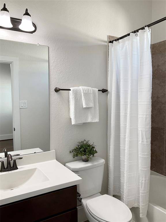 An ensuite bathroom features a clean, modern design with neutral-toned tiles surrounding a bathtub. It includes a white countertop with a sleek faucet, a large mirror, and a small window for natural light. A towel rack and simple decor add a touch of elegance.