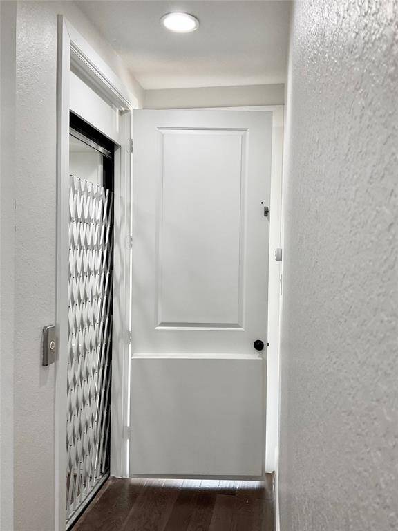 The third floor elevator hallway from the primary bedroom to the secondary bedroom.  the washer and dryer are conveniently located in between the two rooms and adjacent from the elevator that offers a retractable security gate, wood flooring, and recessed lighting.