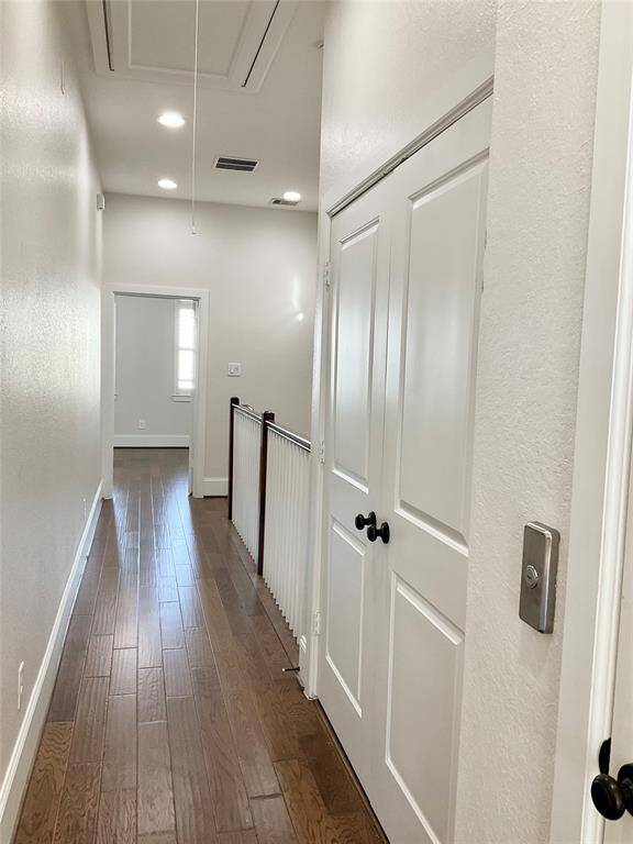 A bright, hallway with wood flooring, recessed lighting, and white walls. It features a double-door entry to the washer and dryer and is located close to the elevator but conveniently between the two secondary bedrooms on the 3rd floor.