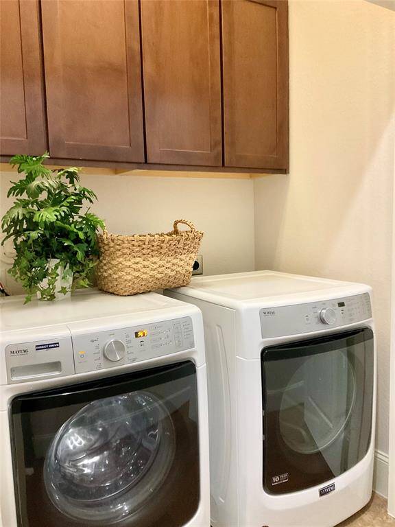 The laundry room featuring modern front-loading washer and dryer units. Above them are wooden cabinets providing additional storage.  The washing machine are is conveniently located between the primary and secondary bedrooms on the third floor.