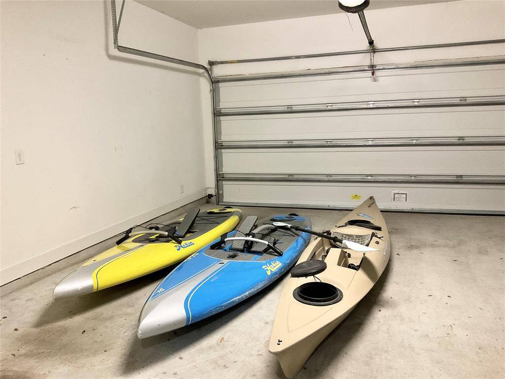 A spacious garage with a clean, white interior, featuring a large closed garage door. The floor is concrete, and there is ample space for your play toys to enjoy Lake Woodlands. East Shore is the heart of The Woodlands and home of the Iron Man ltriathalon.  Endless walking trails, wildlife, entertainment and fabulous dining.