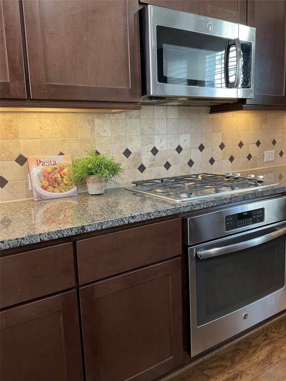 Modern kitchen with dark wood cabinets, granite countertops, and stainless steel appliances, including a microwave and oven. The tiled backsplash adds a stylish touch.