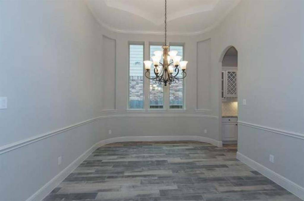 Bright dining area with elegant chandelier, high ceiling, and large windows. Features wood-style flooring and an arched entryway leading to additional space.