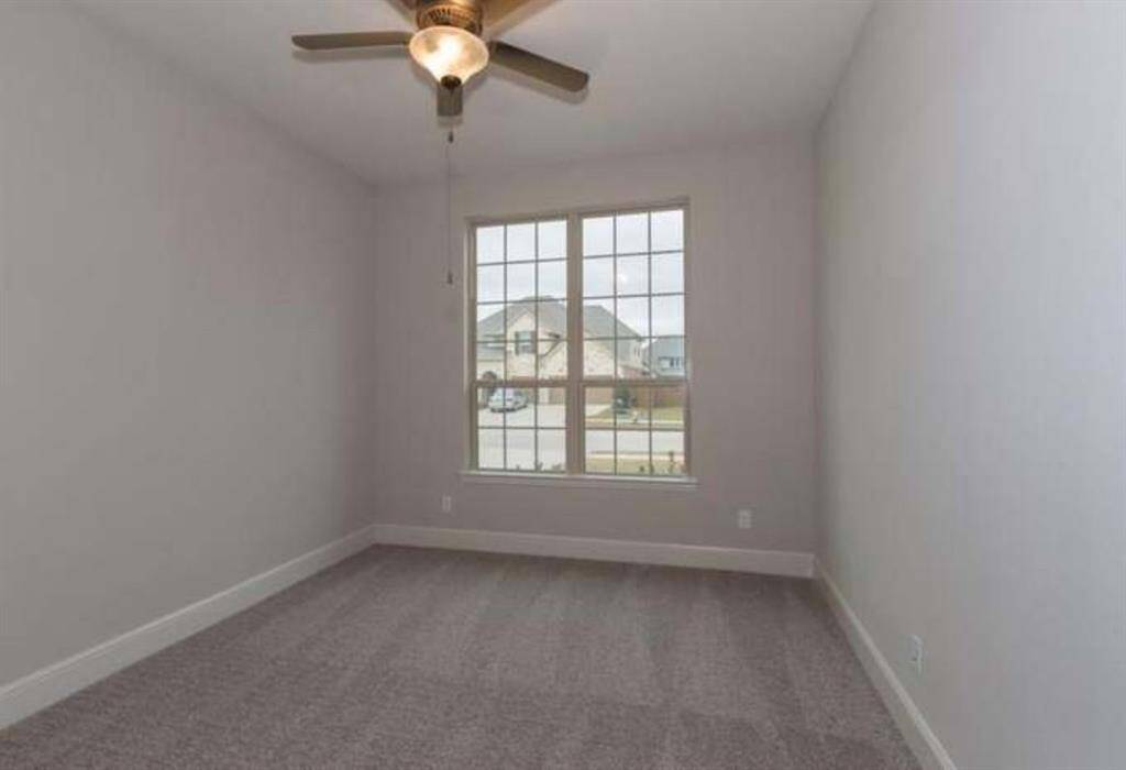 This room features neutral walls, plush carpet, and a large window providing ample natural light. A ceiling fan adds comfort and style. Ideal for a bedroom or home office.