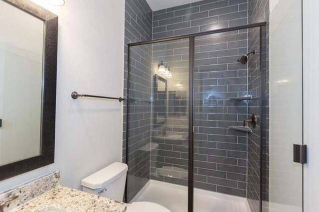 Modern bathroom with a sleek glass-enclosed shower featuring dark subway tiles. The space includes a granite countertop, a contemporary mirror, and a clean, minimalist design.