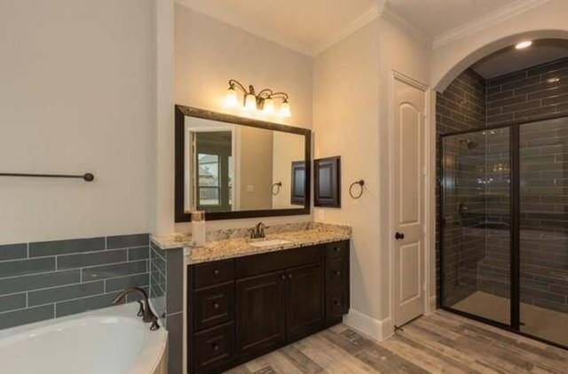 This bathroom features a modern design with a granite countertop and dark wood vanity. It includes a spacious walk-in shower with glass doors and a separate bathtub. The floor is finished with light wood-style tiles, and soft lighting adds warmth to the space.
