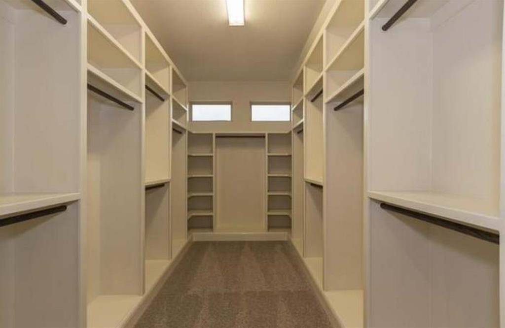 Spacious walk-in closet with ample shelving and hanging space, featuring a neutral color scheme and overhead lighting for a bright, organized feel.