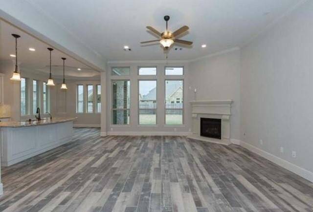 Spacious and filled with natural light, this inviting living area features modern wood-look tile flooring, elegant plantation shutters, a cozy corner fireplace, and an open-concept layout that flows into a stylish kitchen with pendant lighting — perfect for both everyday living and entertaining.