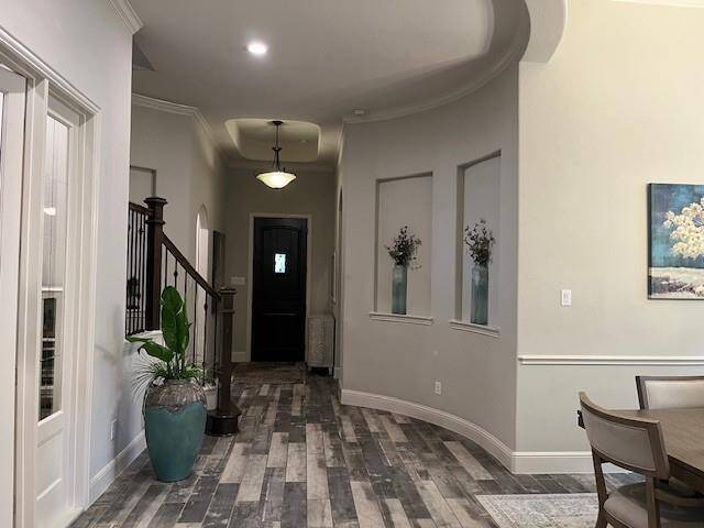 A well-lit entryway with elegant wood-style flooring and a curved wall. The staircase features a dark railing. There's a dining area, creating an inviting, open space.