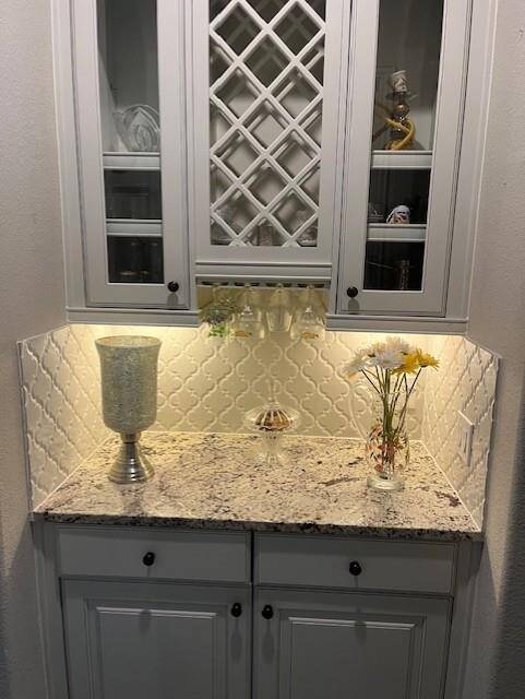 Charming butler’s pantry featuring elegant white cabinetry with glass-front doors, a built-in wine rack, and under-cabinet lighting that highlights the intricate arabesque tile backsplash. The granite countertop provides a luxurious workspace or serving area.