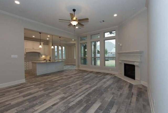This spacious living area features modern wood-look flooring, a cozy fireplace, and large windows offering natural light. The open layout seamlessly connects to a stylish kitchen with an island and pendant lighting, creating a perfect space for entertaining.