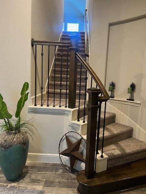 Elegant staircase with rich wood accents and wrought iron spindles, creating a warm and sophisticated entry to the upper level. The neutral-toned carpeting adds comfort and contrast, while the decorative niche with modern planters adds a stylish touch.